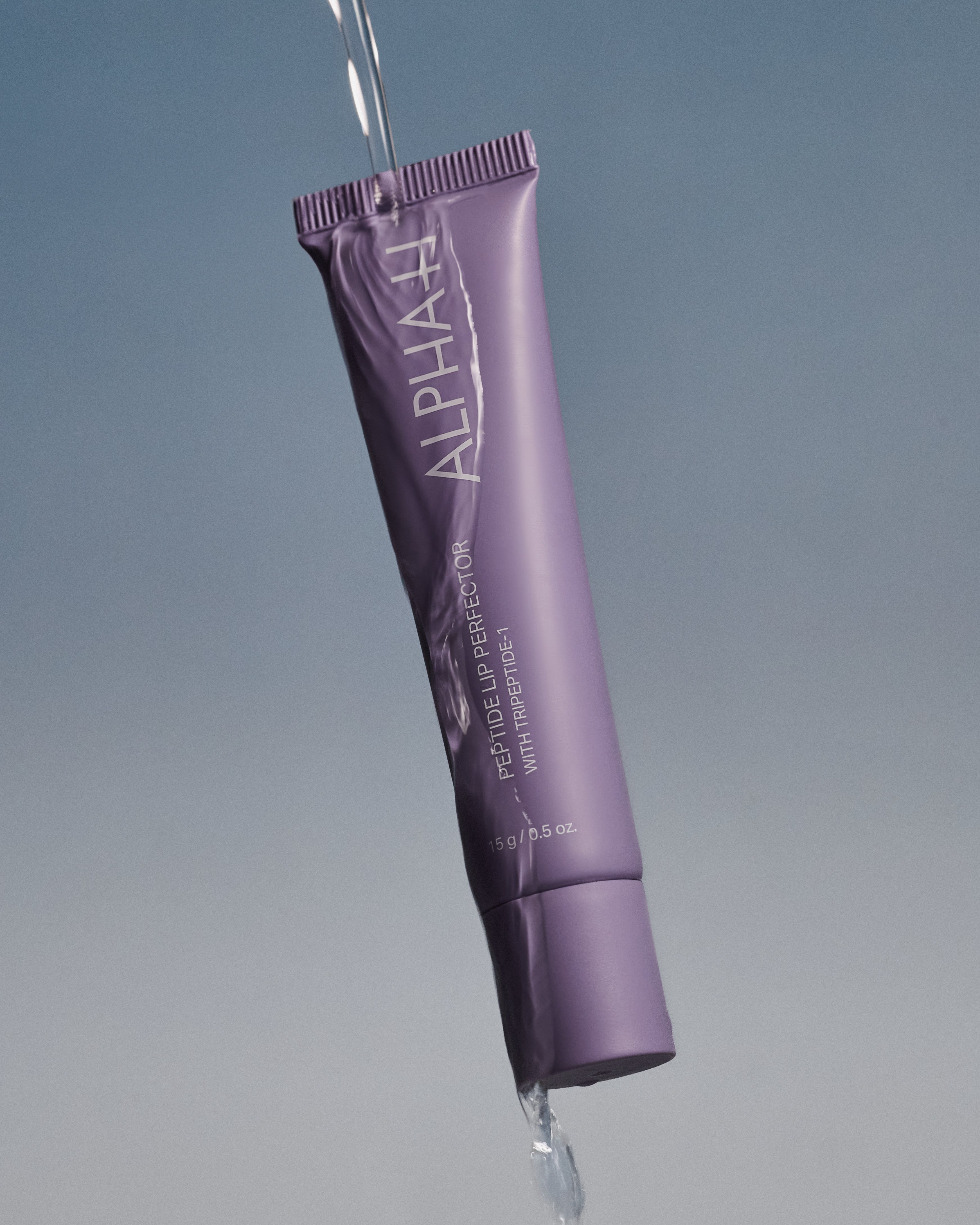 Purple Alpha-H lip balm tube of Peptide Lip Perfector on a blue background